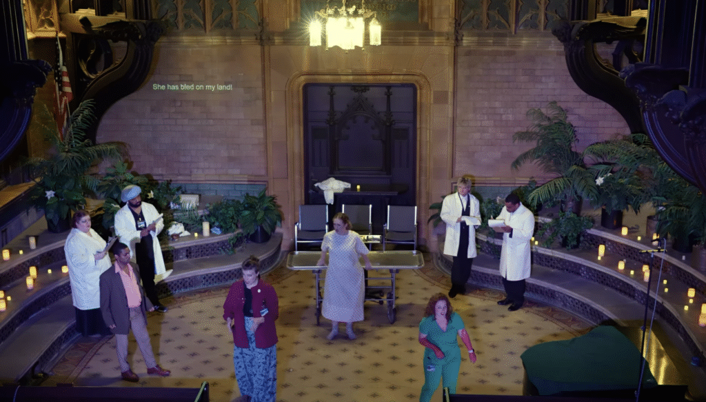 A photograph of The Harbingers, showing the Soul in the center of a room full of patients and doctors